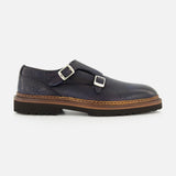 The Mezzaro Bisonte Loafer by DI BIANCO features dark blue bison leather with double monk straps, two silver buckles, a brown midsole, and a black rubber outsole, displayed in profile against a plain white background.