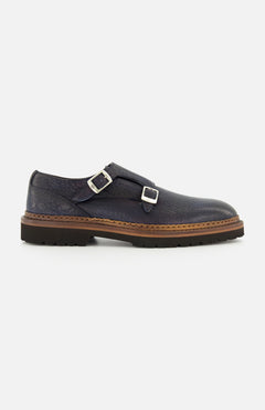The Mezzaro Bisonte Loafer by DI BIANCO features dark blue bison leather with double monk straps, two silver buckles, a brown midsole, and a black rubber outsole, displayed in profile against a plain white background.