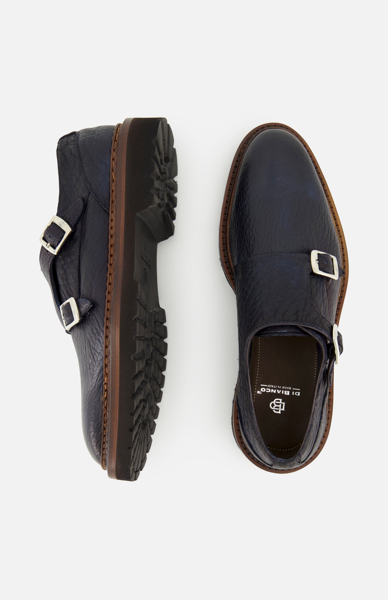 The Mezzaro Bisonte Loafer by DI BIANCO, crafted from dark blue bison leather, features double monk straps with silver buckles and brown soles. The shoes are displayed from the top and side on a white background.