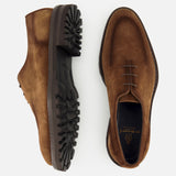 A pair of DI BIANCO Marche Suede Loafers in hand-stitched, light brown suede with dark, rugged rubber soles. One loafer is displayed from the side and the other from the top, both featuring visible stitching and laces that highlight their Italian craftsmanship.