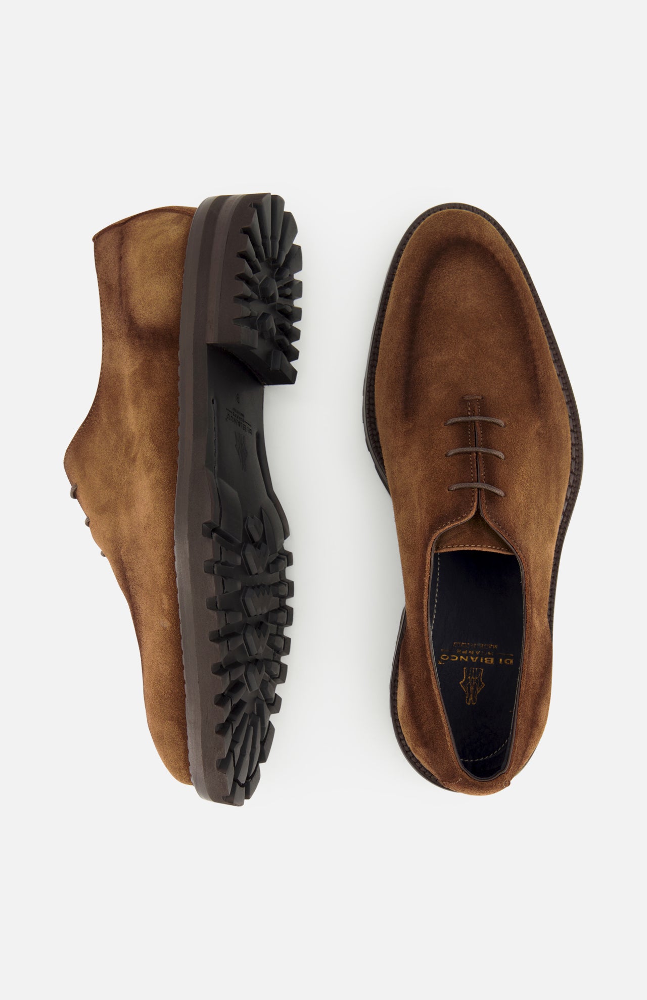 A pair of DI BIANCO Marche Suede Loafers in hand-stitched, light brown suede with dark, rugged rubber soles. One loafer is displayed from the side and the other from the top, both featuring visible stitching and laces that highlight their Italian craftsmanship.