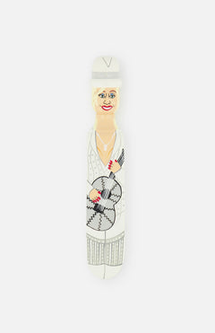 The ‘Doll’ Wood Door Stopper by WEDGIE is inspired by Dolly Parton, featuring an illustration of a smiling woman in a white outfit and hat, holding a guitar, with red lipstick and nails.