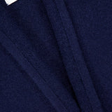 Close-up of a dark blue textured fabric with visible seams and a white label that reads ELDER STATESMAN, evoking the luxurious Italy Cashmere Smoking Cardigan with its refined shawl collar.