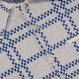 Close-up of the Nimbus Plaid Button Up Knit Overshirt by ELDER STATESMAN, featuring a beige knit design with blue plaid patterns, tan buttons, and a visible ELDER STATESMAN label.