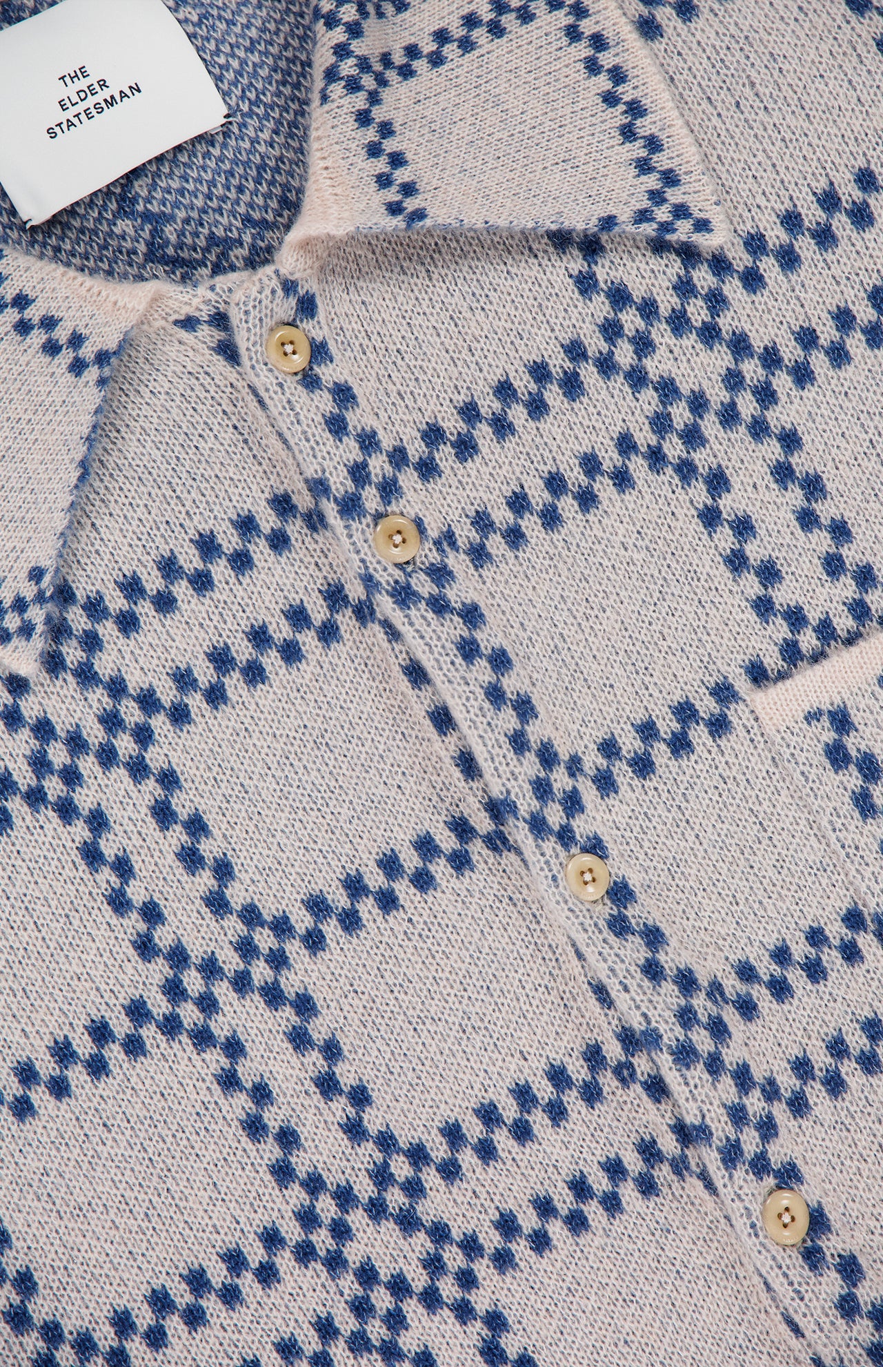 Close-up of the Nimbus Plaid Button Up Knit Overshirt by ELDER STATESMAN, featuring a beige knit design with blue plaid patterns, tan buttons, and a visible ELDER STATESMAN label.