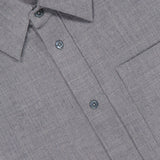 Close-up of the Pashmina Big Button Up Shirt by ELDER STATESMAN in light grey, featuring a classic collar, chest pocket, and four visible buttons. A partially visible pink label with text appears at the neckline. Designed as an ideal piece of office wear, the shirt's fabric boasts a soft, textured look reminiscent of luxurious wool cashmere.