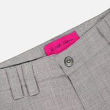 Close-up of the waistband of the ELDER STATESMAN Pashmina Norm Pant in grey, highlighting the button and belt loops, with a bright pink label featuring cursive writing on the inside.