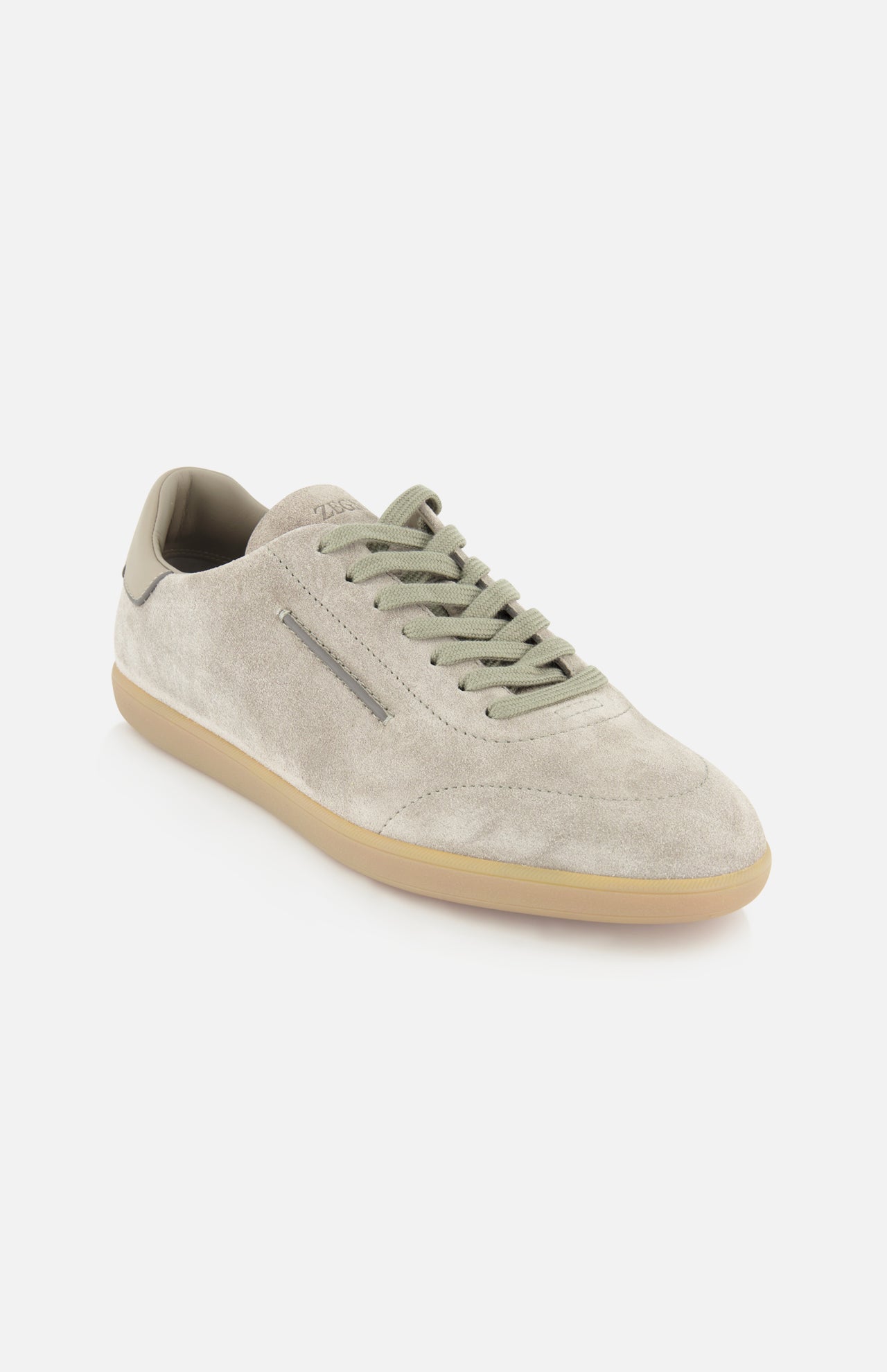 Introducing the ZEGNA 232 Low Top Sneaker: crafted in Italy from beige suede, this elegant footwear features light green laces, a beige rubber sole, and minimal stitching for a refined look. Presented against a white background, the design combines classic inspiration from light grey suede sneakers with modern details, embodying understated sophistication.