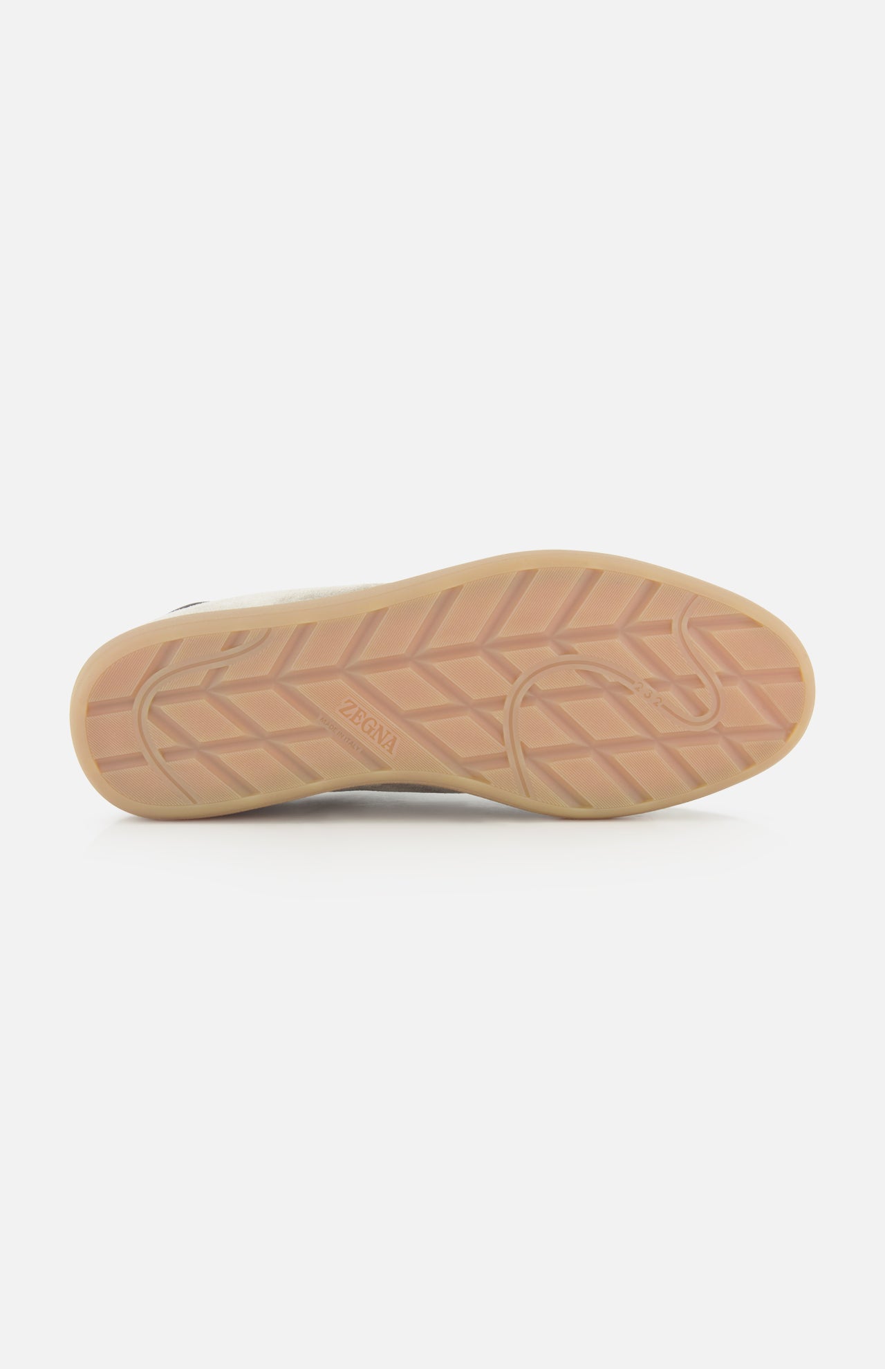 The image displays the sole of the ZEGNA 232 Low Top Sneaker, featuring a light brown color with a geometric tread pattern and “ZEGNA” embossed near the arch. This sole is part of a light grey suede sneaker, expertly crafted in Italy.