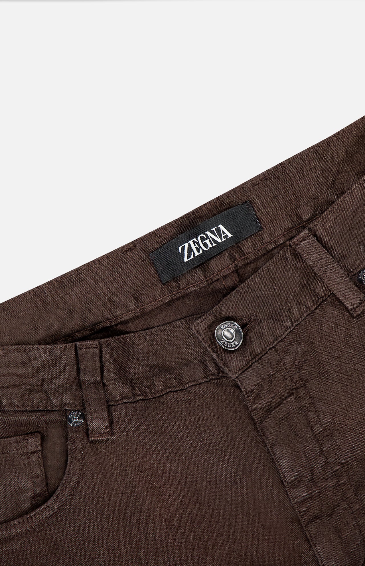 Close-up of the waist area of ZEGNA Comfort Linen Cotton Pants in slim fit, dark brown, showcasing a visible ZEGNA label, belt loops, button closure, and detailed front pockets.
