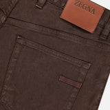 Close-up of the back pocket and waistband of ZEGNA Comfort Linen Cotton Pants in slim fit, dark brown, featuring a tan leather patch with the brand name above the pocket.