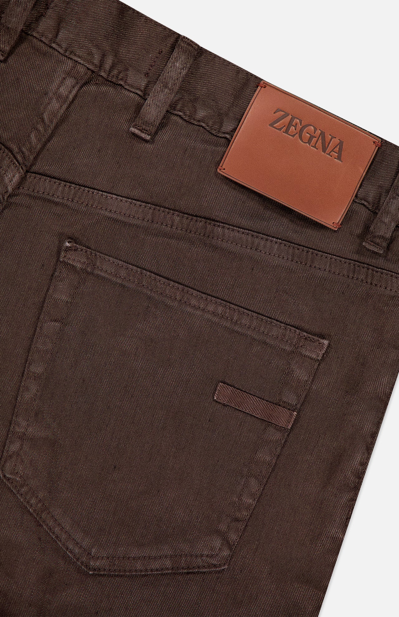 Close-up of the back pocket and waistband of ZEGNA Comfort Linen Cotton Pants in slim fit, dark brown, featuring a tan leather patch with the brand name above the pocket.
