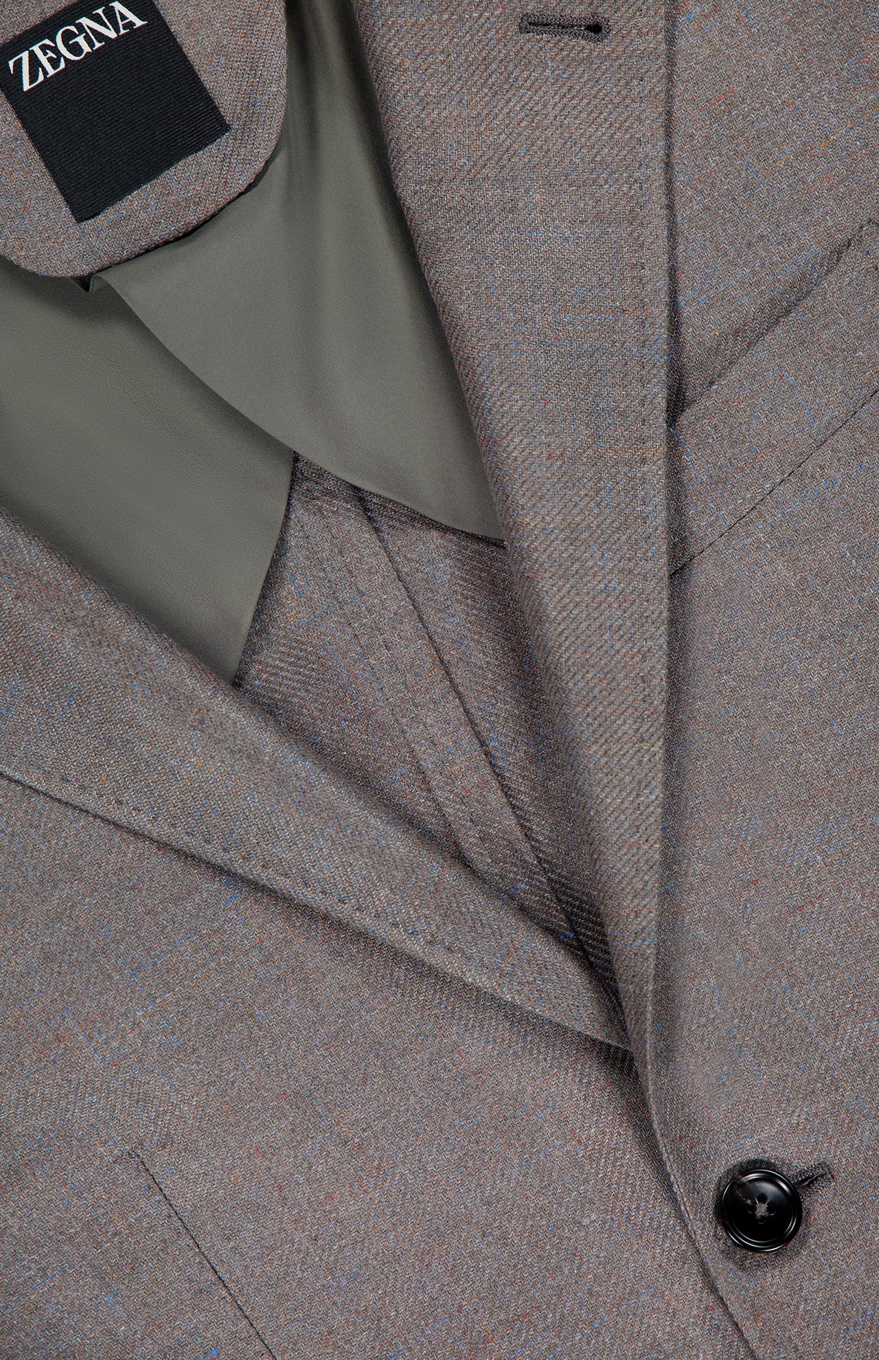 Close-up of a neatly folded ZEGNA Detachable Knit Bib Sportcoat, showcasing its sleek design, signature label, dark button, and a hint of olive green lining.