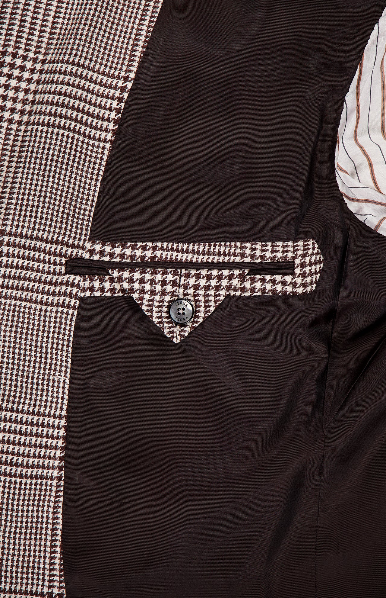 Close-up of the ZEGNA Houndstooth Plaid Linen-blend Sportcoat’s interior, featuring a buttoned pocket, brown lining, and brown-and-white striped fabric—a classic detail for any men's professional wardrobe.