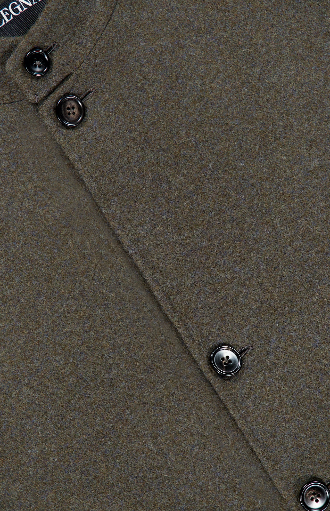 Close-up of the ZEGNA Jerseywear Chore Jacket in brown, showcasing four dark buttons and a subtly angled silhouette. The partially visible fabric label appears at the top left corner. The jacket is crafted from textured, soft material with precise stitching—capturing the refined essence of a classic wool cashmere design.