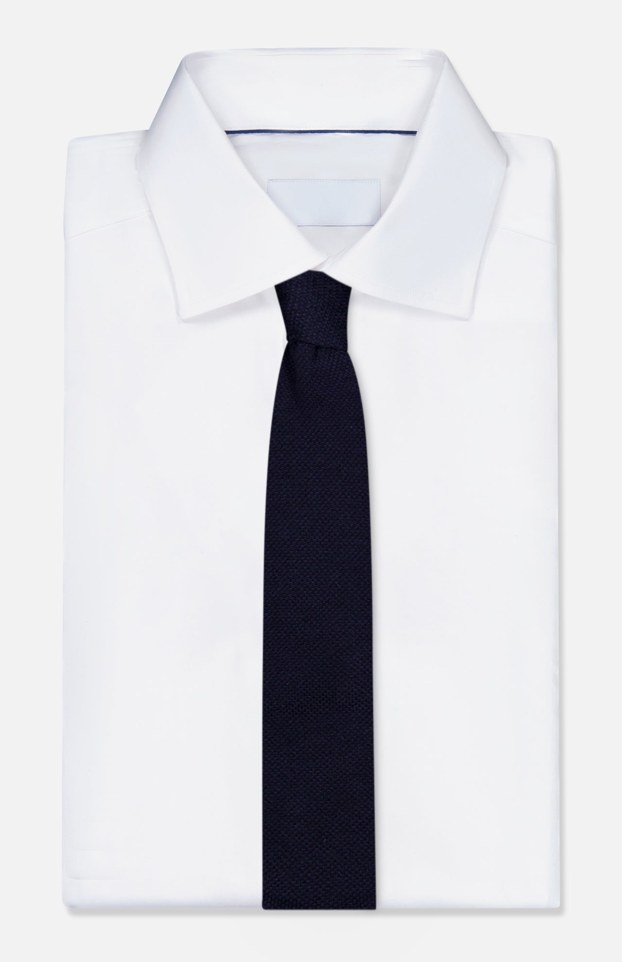 A neatly folded white dress shirt with a classic collar is paired with the ZEGNA Oasi Cashmere Knit Tie, showcasing its refined navy design, all displayed against a plain white background.