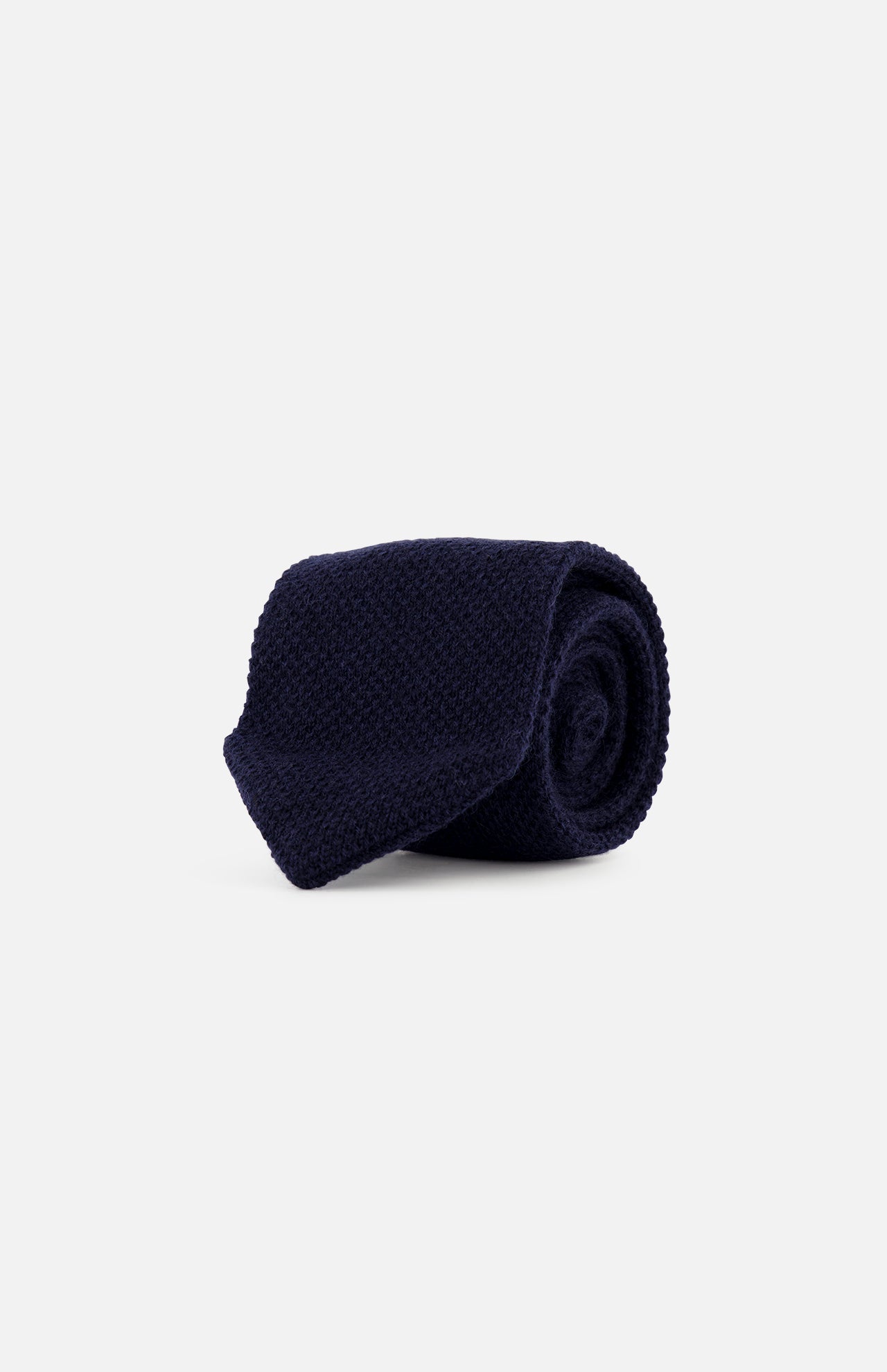 A rolled-up Oasi Cashmere Knit Tie in dark navy blue, featuring a refined knit design, is displayed on a plain light gray background. Expertly crafted in Italy by ZEGNA, this accessory embodies timeless elegance and superior craftsmanship.