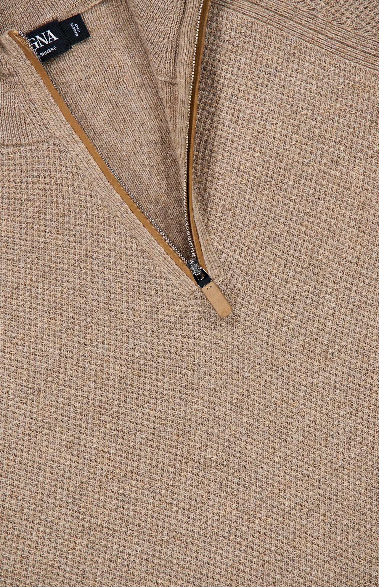 Close-up of the ZEGNA Oasi Cashmere Zip Mockneck Sweater in beige, featuring a textured Italian cashmere knit and a partially unzipped brown zipper. A black brand tag is visible near the collar.