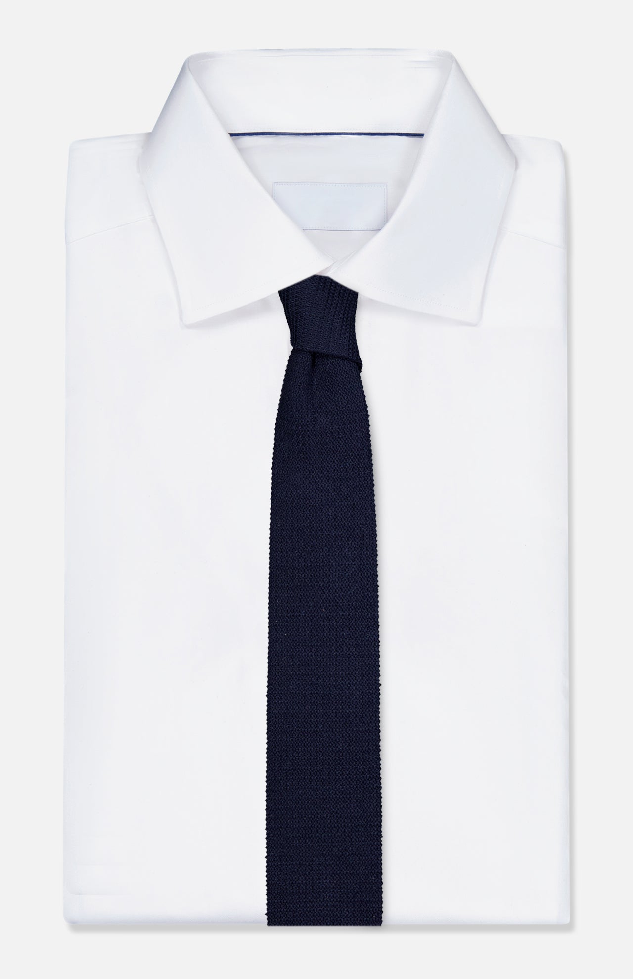 A crisp white dress shirt with a pointed collar is paired with the ZEGNA Oasi Lino Knit Neck Tie in dark navy, displayed on a plain white background.