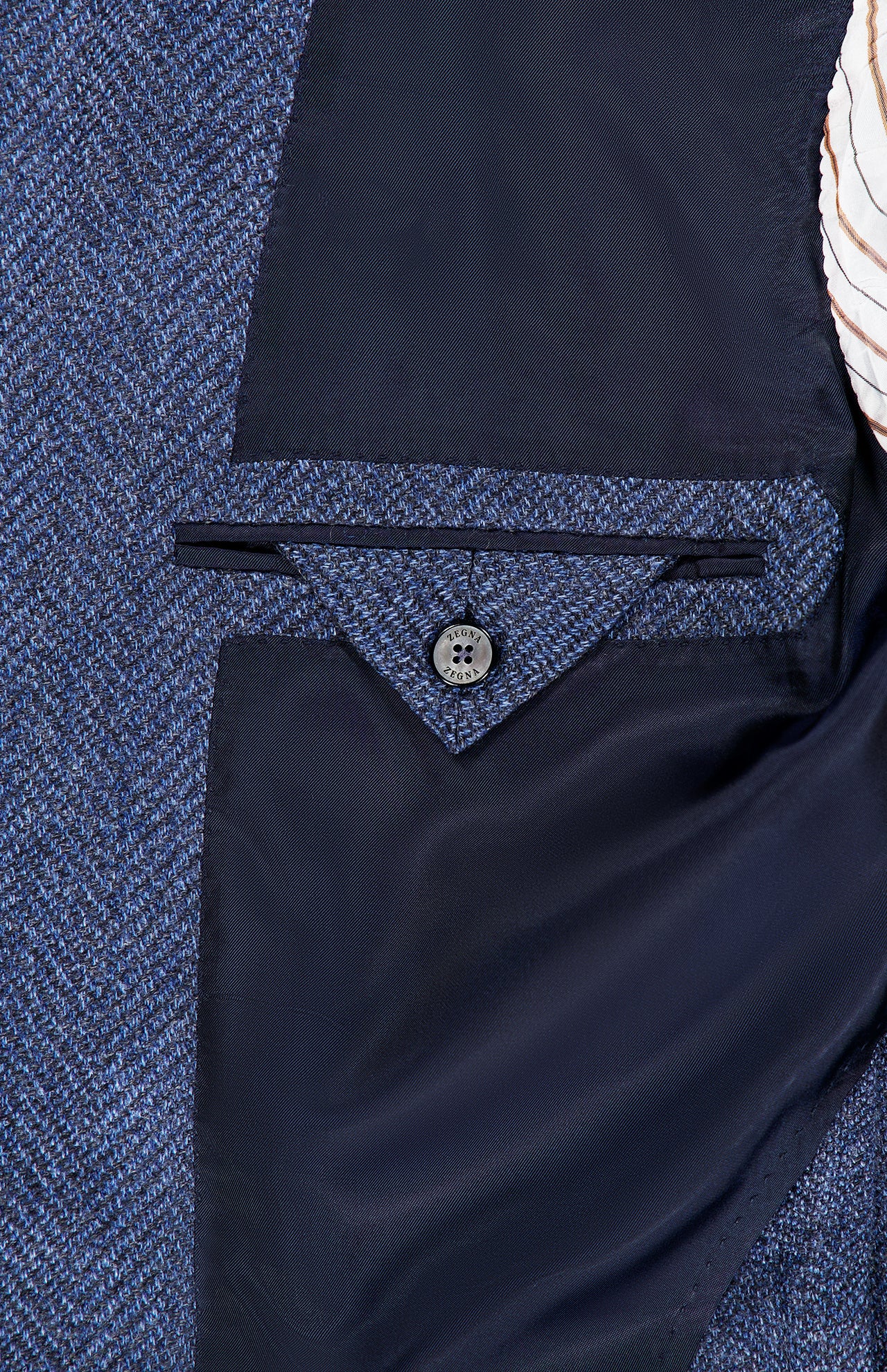 Close-up of the inside pocket of the ZEGNA Pure Cashmere Sportcoat in dark blue, tailored in classic tweed with a button closure and dark lining, shown next to a white and brown striped shirt.