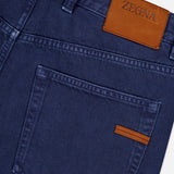 Close-up of the back of ZEGNA Pure Cotton Slim Fit Pants in blue, with a brown leather ZEGNA logo patch above the right pocket, a small brown pocket accent, and classic 5-pocket styling.