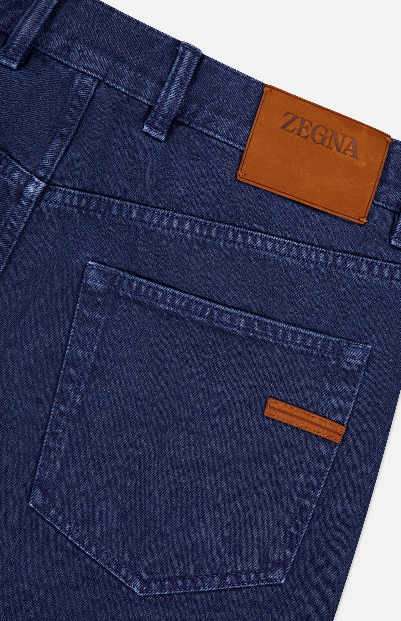 Close-up of the back of ZEGNA Pure Cotton Slim Fit Pants in blue, with a brown leather ZEGNA logo patch above the right pocket, a small brown pocket accent, and classic 5-pocket styling.