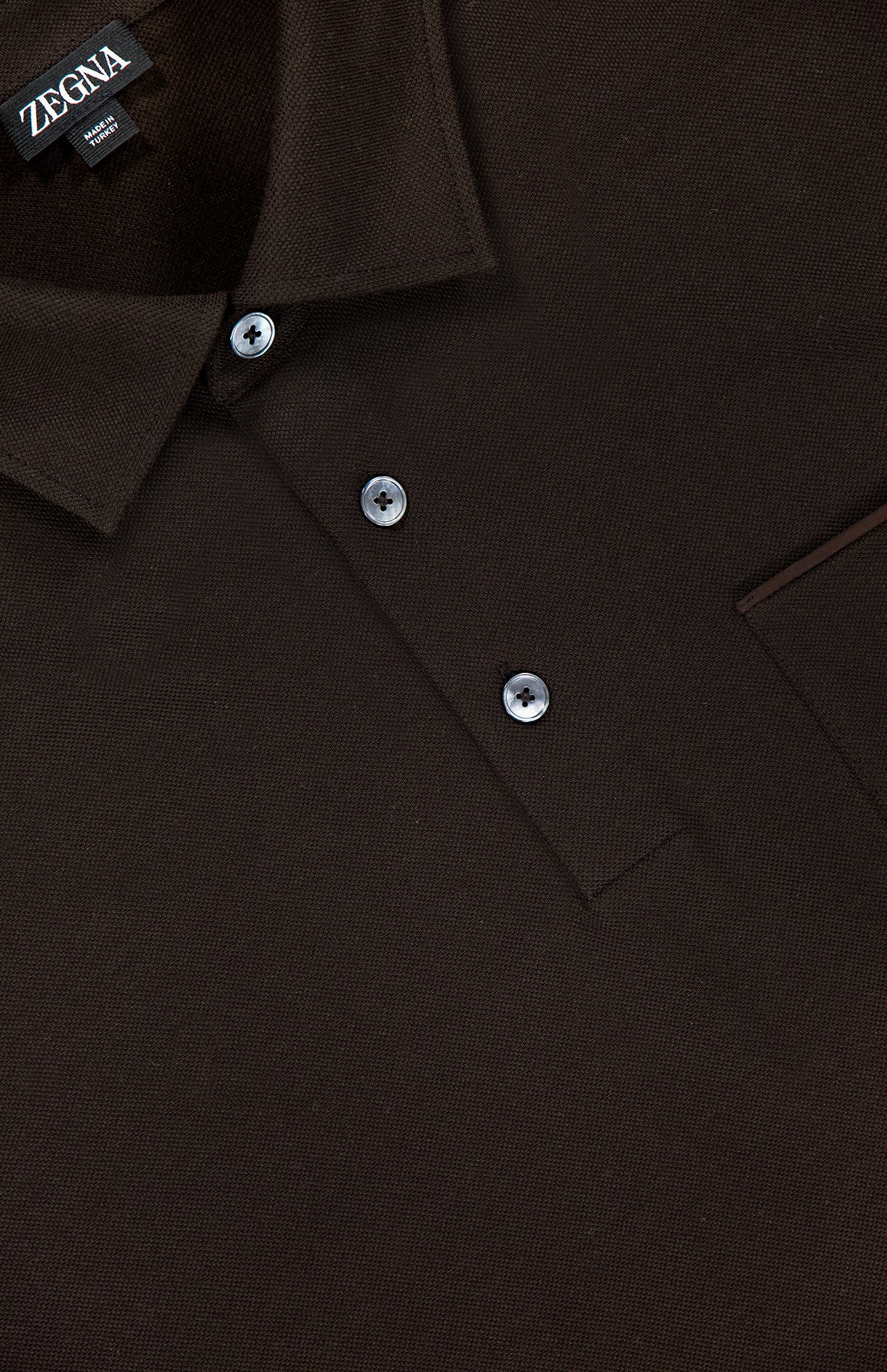 A close-up of the ZEGNA Pure Cotton Piquet Short Sleeve Polo Shirt in dark brown, highlighting the collar, three buttons, part of the chest pocket, and the ZEGNA label at the neckline.