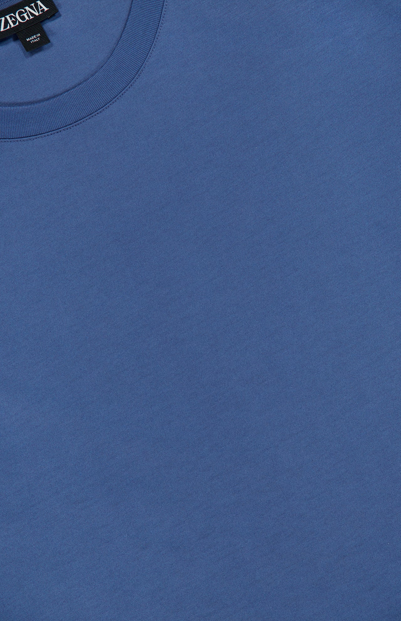 Close-up of a blue Pure Cotton T-Shirt by ZEGNA in 100% cotton with a relaxed fit and a visible black ZEGNA label at the neckline, shown on a flat surface.