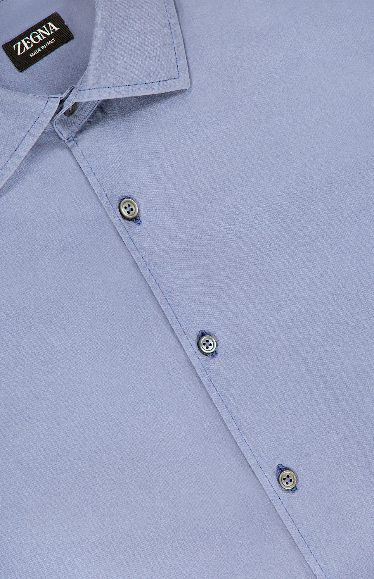 A close-up of the ZEGNA Pure Silk Dress Shirt in blue, featuring a visible brand label on the collar and three front buttons. The smooth fabric is neatly pressed and made in Italy.