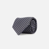 The ZEGNA Silk Jacquard Tie, crafted in Italy from luxurious silk and featuring a small repeating yellow and white geometric pattern on navy blue, is displayed rolled up against a plain white background.