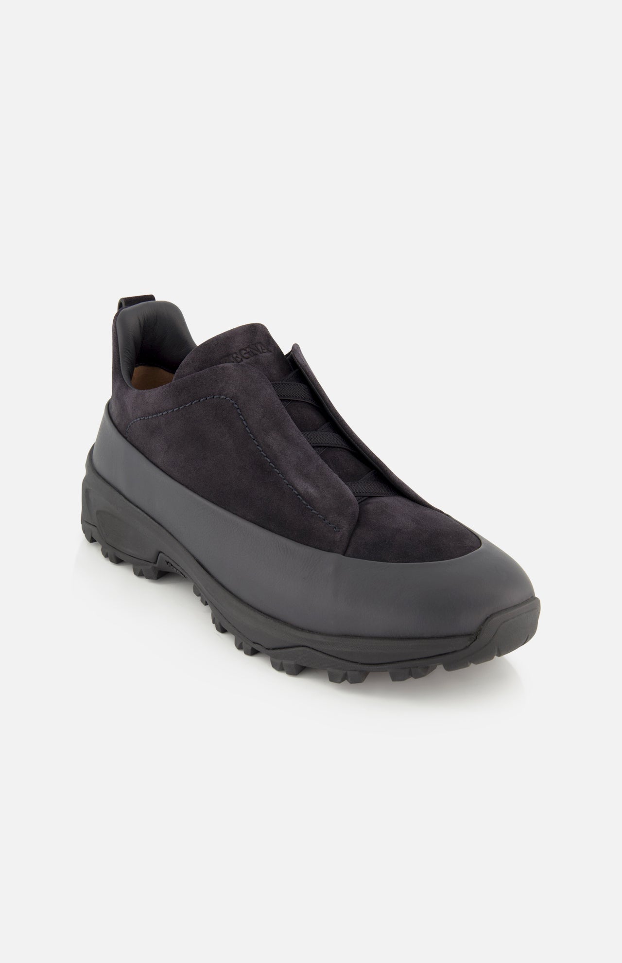 The ZEGNA Triple Stitch Low Top Sneaker is a black, hiking-inspired slip-on with a suede upper and minimal detailing, set atop a thick rubber sole. The shoe is photographed against a plain white background.