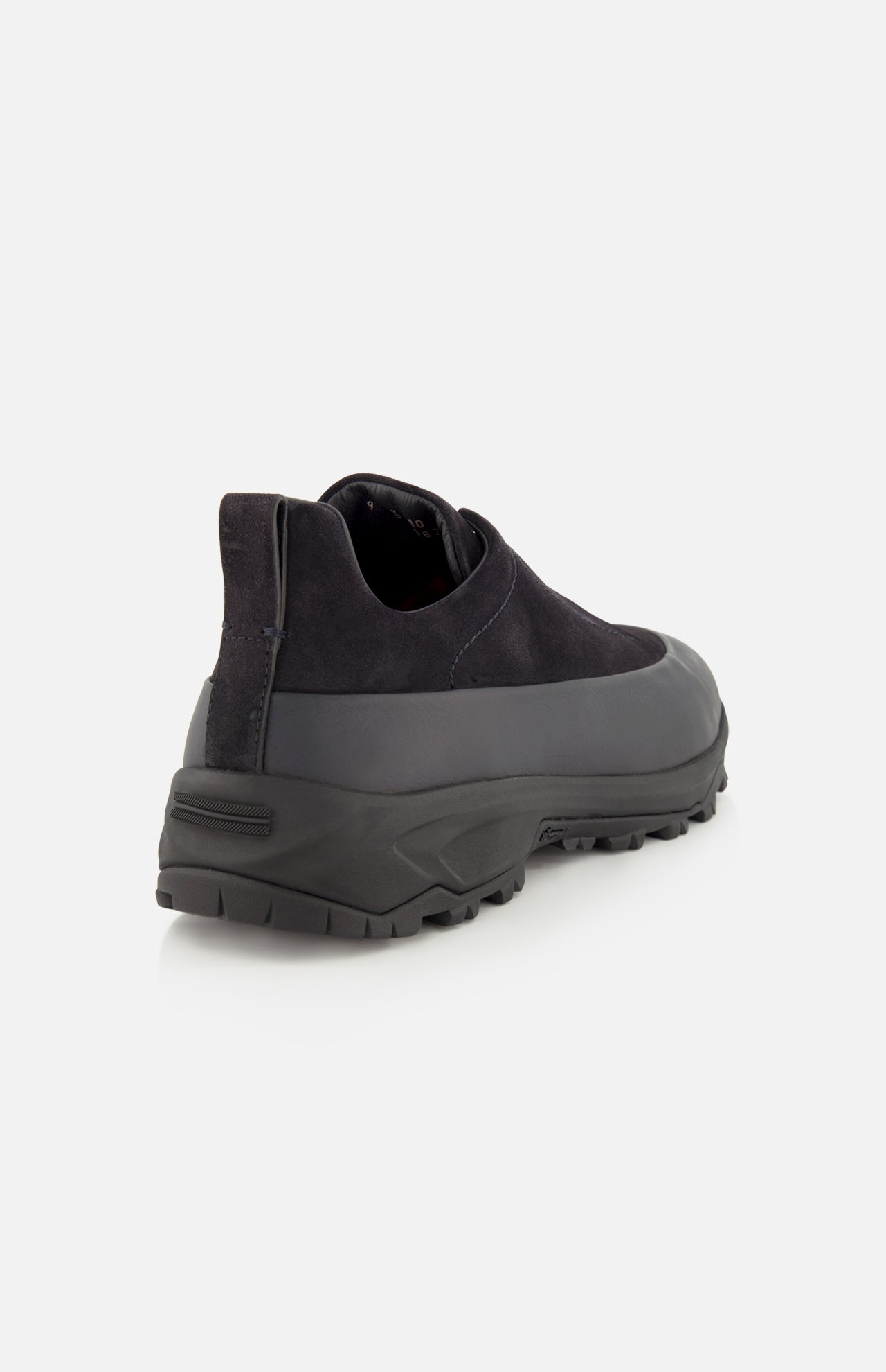 The ZEGNA Triple Stitch Low Top Sneaker is a black, hiking-inspired shoe with a slip-on design, featuring a thick, rugged sole and a smooth upper. It is displayed from the rear angle on a plain white background.