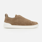 The ZEGNA Triple Stitch Low Top Sneaker, featuring brown suede uppers and a white rubber sole, is shown in a side view against a plain white background, exemplifying luxury casual footwear.