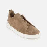 The ZEGNA Triple Stitch Low Top Sneaker features brown suede in a slip-on design with a white rubber sole and minimal stitching details inspired by luxury casual footwear, photographed against a plain white background.