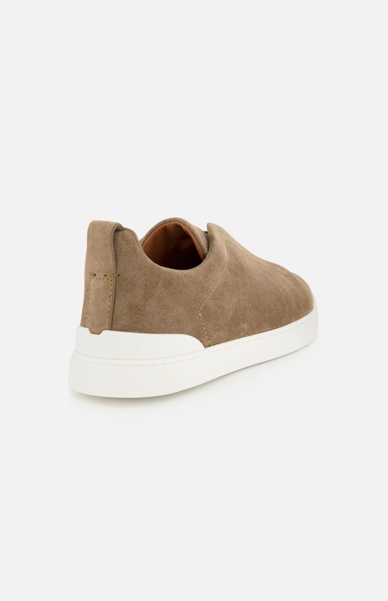 A luxurious casual footwear choice, the tan suede ZEGNA Triple Stitch Low Top Sneaker is showcased from the back and slightly to the side against a plain white background, highlighting its sleek white rubber sole.