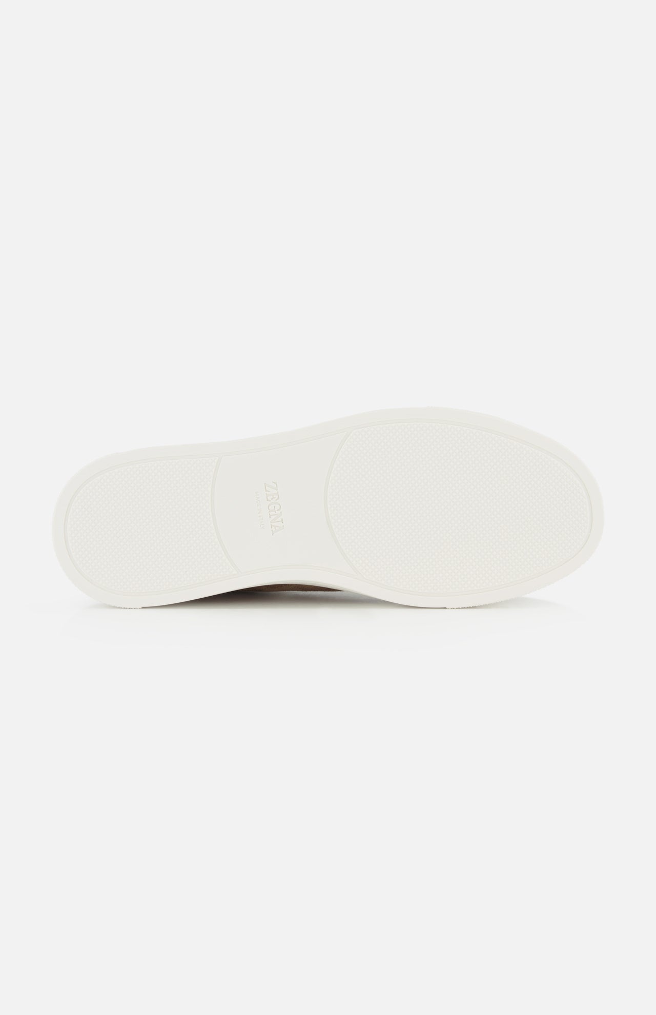 The image features the bottom view of a white ZEGNA Triple Stitch Low Top Sneaker sole set against a plain white background. The sole displays a subtle texture and gentle contouring for enhanced grip, showcasing the refined design characteristic of luxury casual footwear.