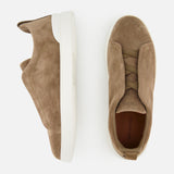 A pair of ZEGNA Triple Stitch Low Top Sneakers in taupe suede with white soles, displayed from the side and top views on a white background, exemplifies luxury casual footwear.