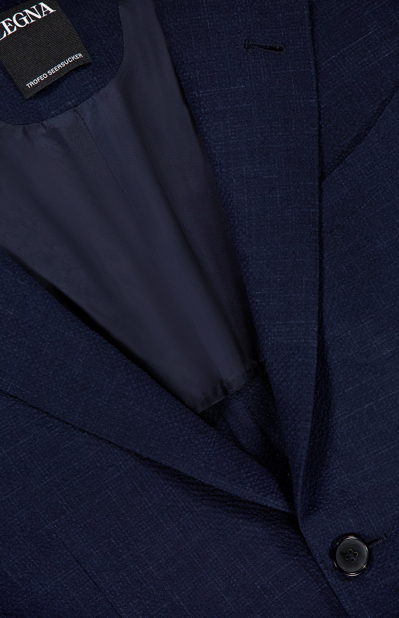 Close-up of the ZEGNA Trofeo Seersucker Suit Jacket in dark navy, featuring seersucker fabric, a single button, partial inner lining, and label inside the collar—a refined choice for any men's professional wardrobe.