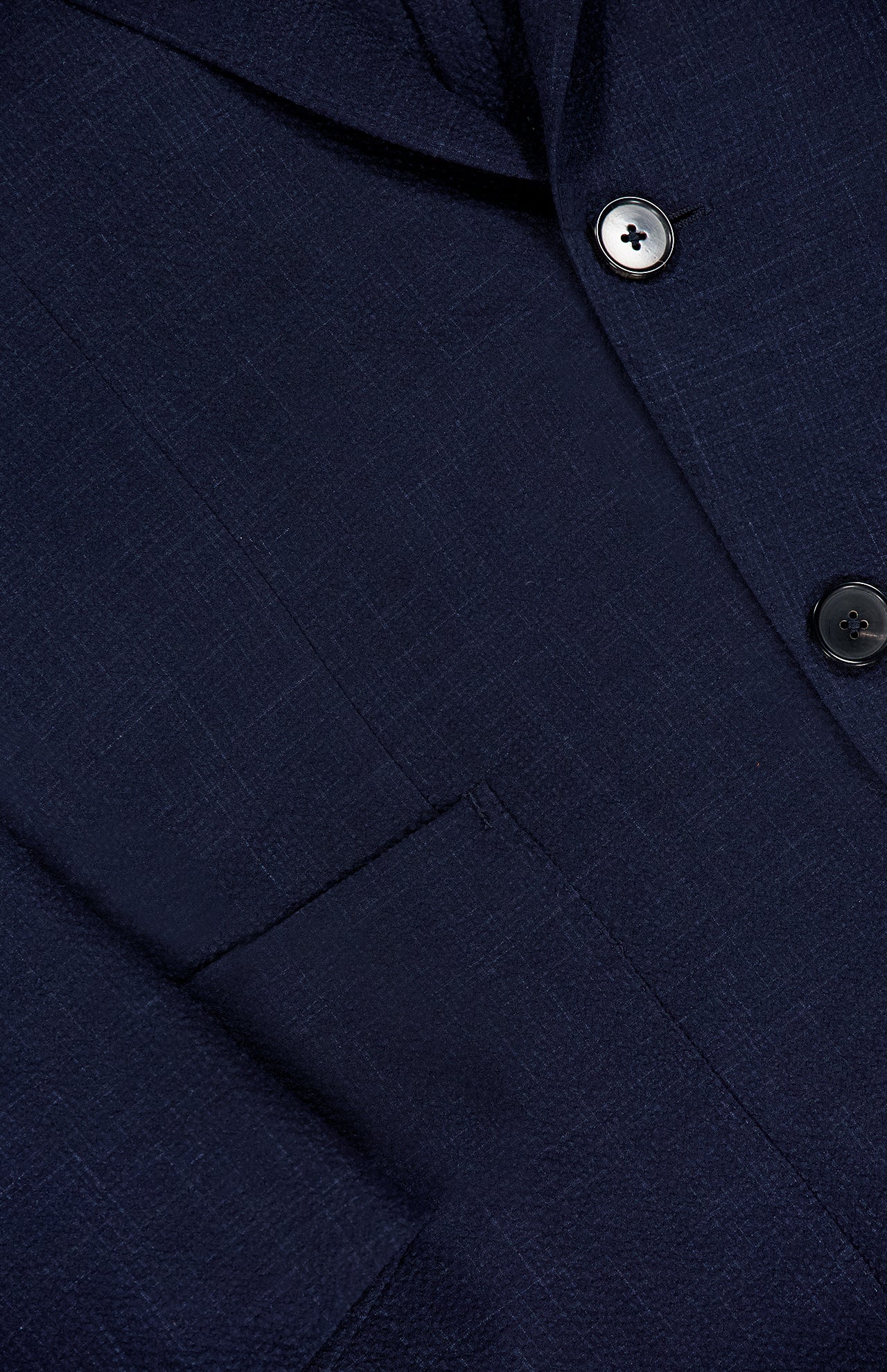 Close-up of the ZEGNA Trofeo Seersucker Suit Jacket in navy, featuring textured fabric, two dark buttons, a front pocket, and part of the lapel—an essential piece for any men's professional wardrobe.