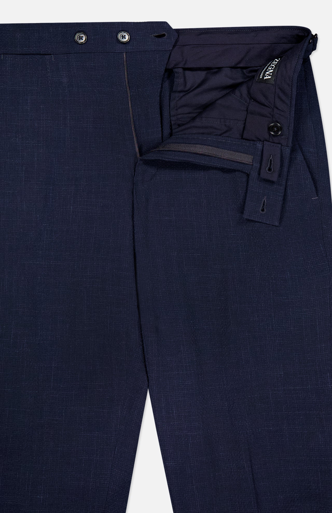 The ZEGNA Trofeo Seersucker Suit Trouser Pant in navy blue showcases textured fabric, partially unzipped and unbuttoned to reveal the waistband, inner lining, closure details, and adjustable side tabs.