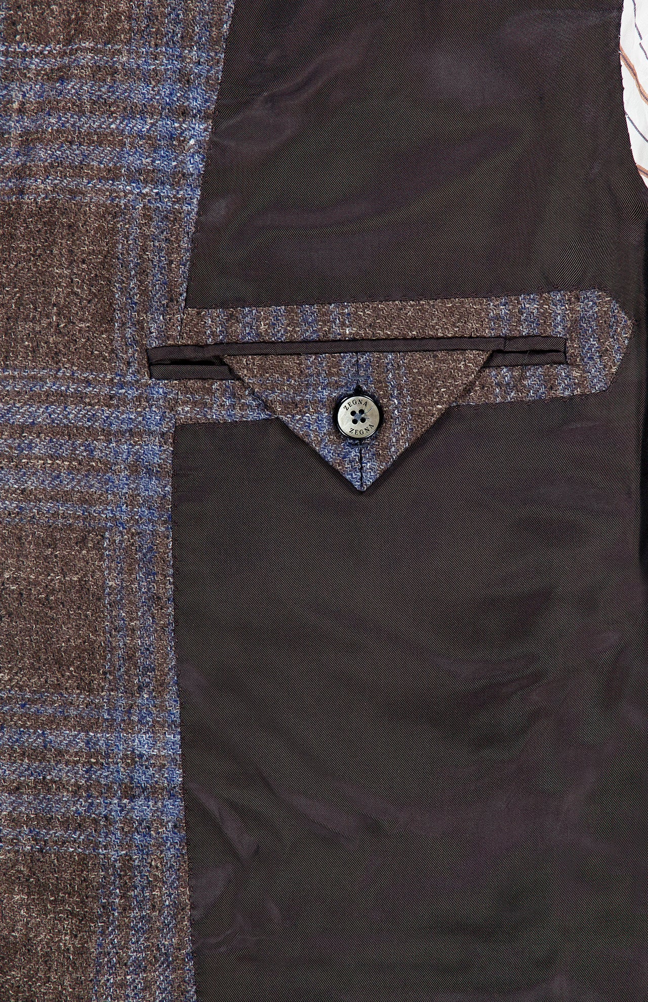 Close-up of the interior of the ZEGNA Wool Silk Linen Sportcoat in brown plaid, featuring a pocket with a flap and button, set against a dark brown silky lining.