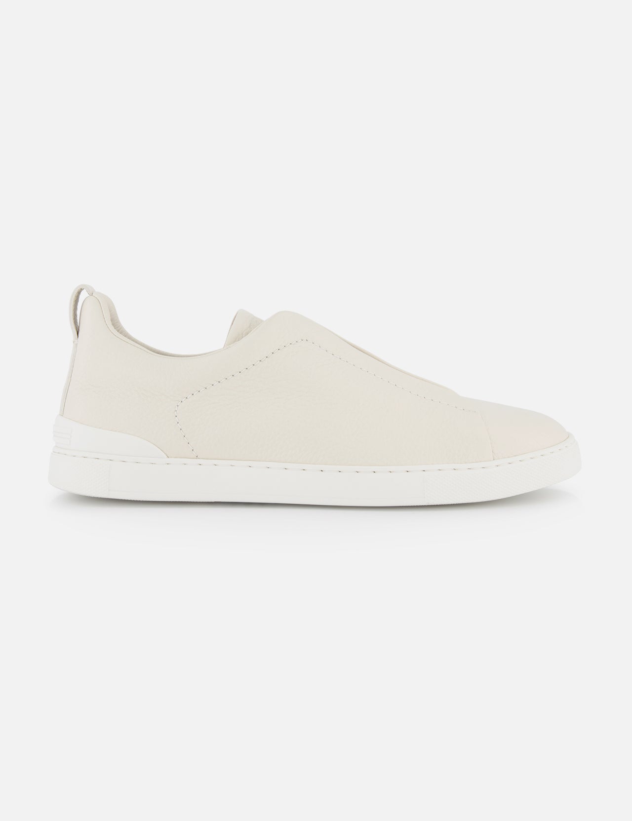A side view of ZEGNA Triple Stitch Sneakers, a minimalist luxury slip-on in light beige with a white rubber sole, photographed on a plain white background.