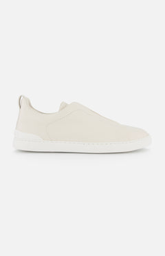 A side view of ZEGNA Triple Stitch Sneakers, a minimalist luxury slip-on in light beige with a white rubber sole, photographed on a plain white background.