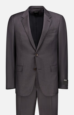 The ZEGNA Trofeo Milano Suit is a dark grey, crease-resistant wool two-piece with notch lapels, two-button closure, and flap pockets. Shown on a plain light background, the jacket is buttoned with trousers placed beneath.