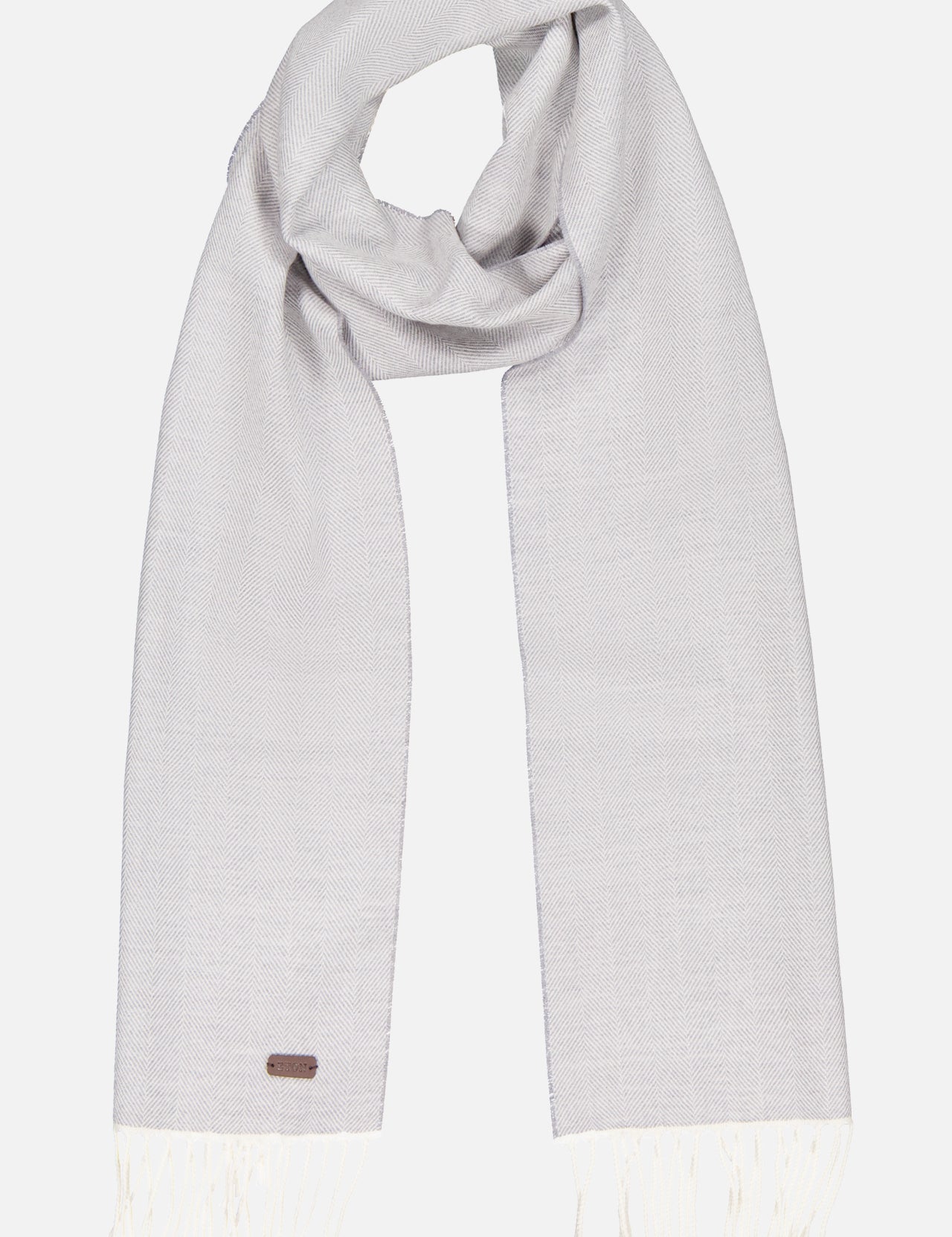 The ETON Herringbone Merino Wool Scarf is light gray with a subtle herringbone pattern, white fringe on both ends, and a small rectangular tag near one edge. Neatly folded, it’s set against a plain white background.