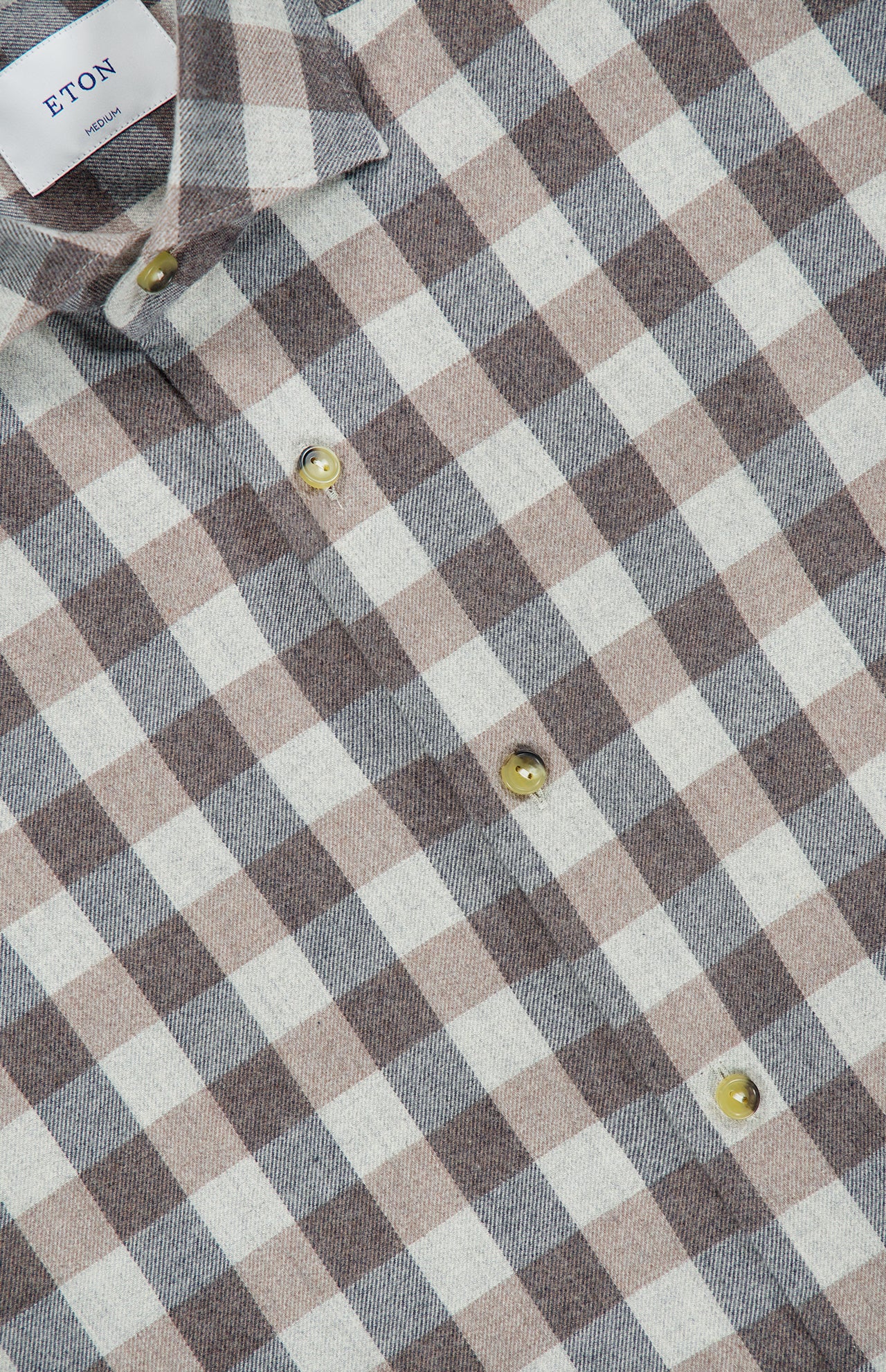 Close-up of ETON’s Block Check Flannel Shirt in brown and white, featuring a pure cotton fabric that accentuates the classic checkered pattern. Yellow buttons provide a distinctive touch, and the collar along with a portion of the ETON label can be seen at the top left of the image.
