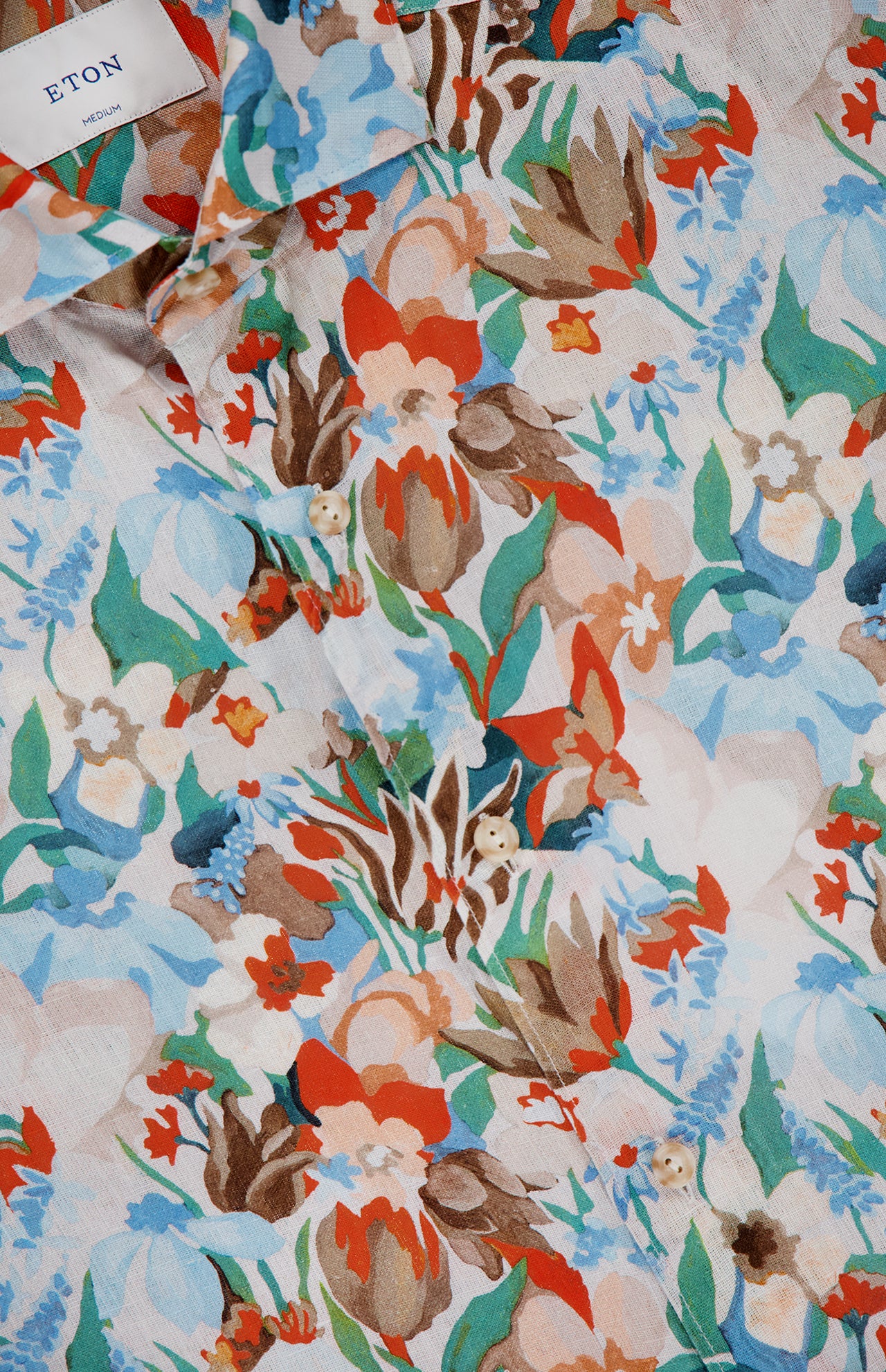 A close-up of the ETON Floral Linen Print Dress Shirt highlights red, blue, green, and beige flowers and leaves on light fabric. The ETON label and buttons are visible on this vibrant orange and blue floral shirt.