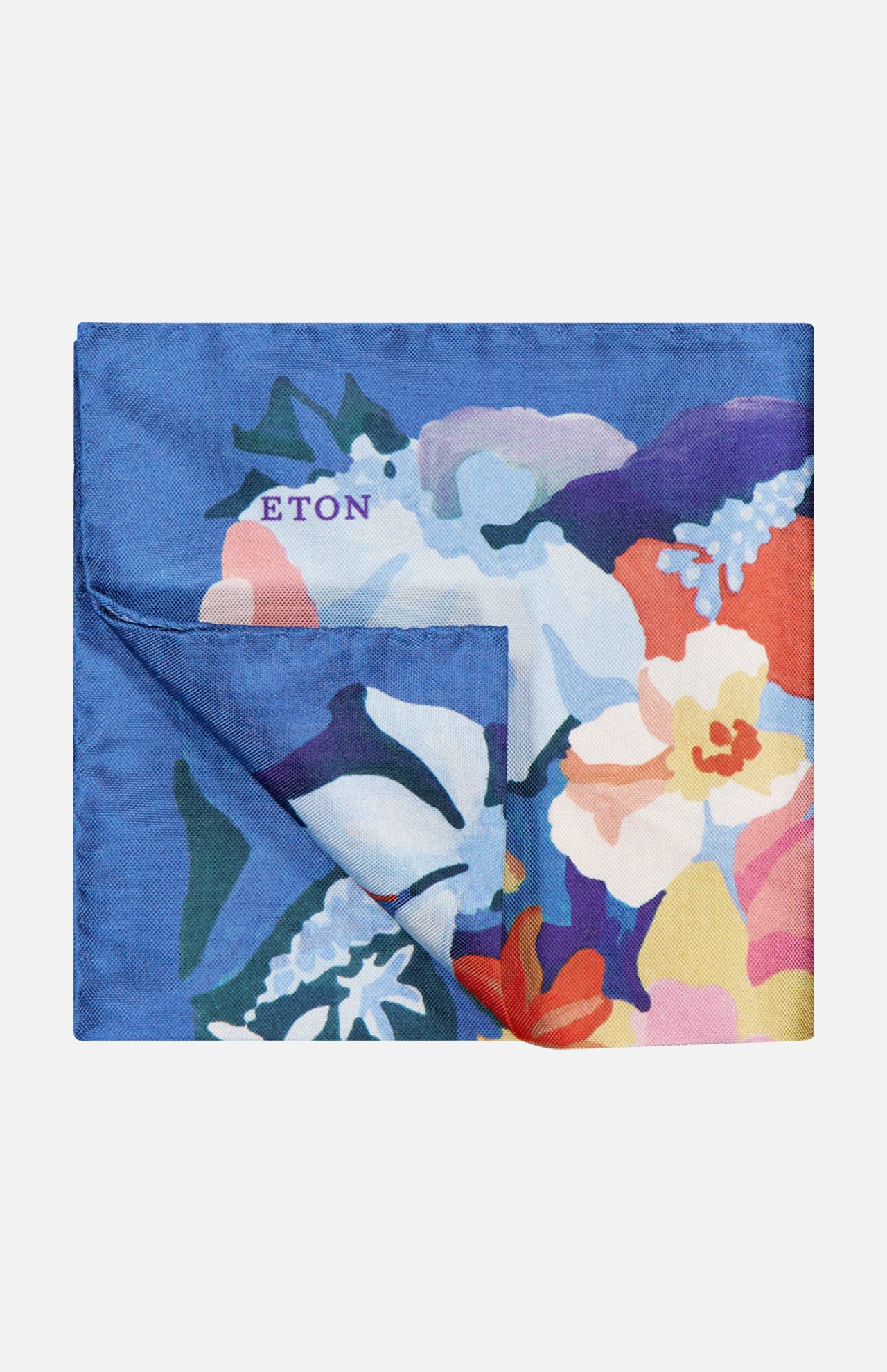 The ETON Floral Oxford Silk Pocket Square features vibrant blue, purple, white, orange, and yellow floral tones on dark blue silk. The word ETON is near the top left, and one corner is folded to reveal its reverse side.