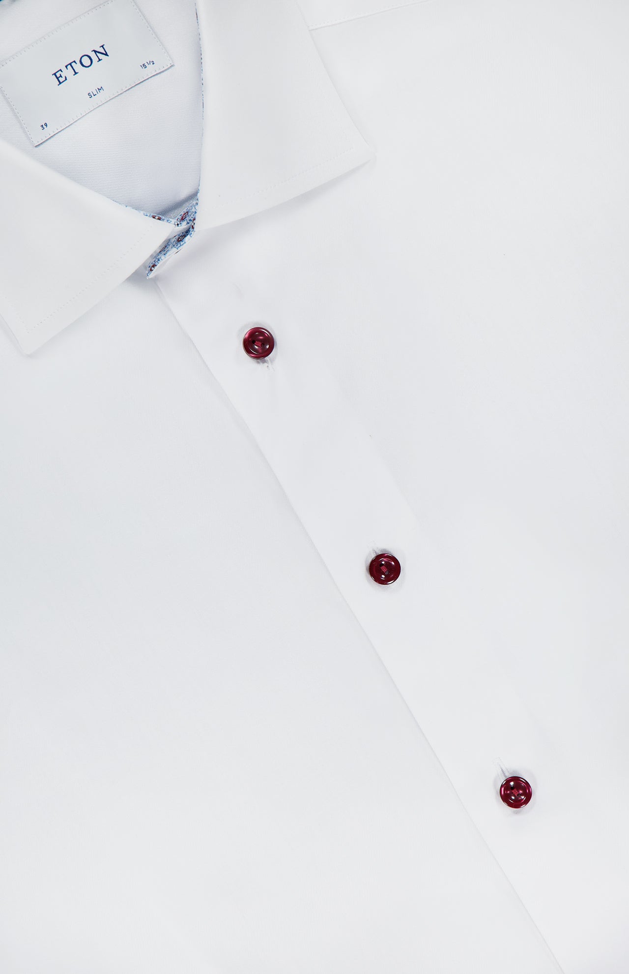 A close-up of ETON’s Geometric Effect Signature Twill Slim Dress Shirt in white, showcasing three maroon buttons, a classic collar, and the partially visible wrinkle-resistant label inside.