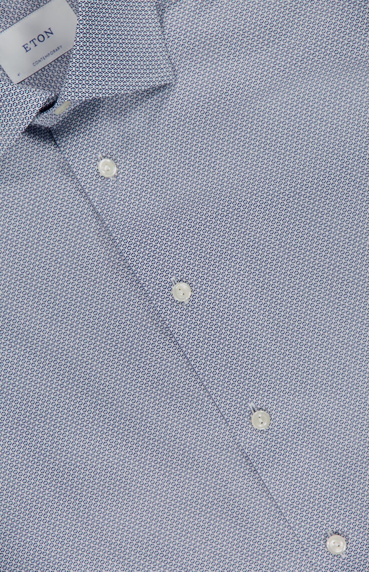 Close-up of ETON's Geometric Signature Twill Dress Shirt in blue, slim fit with a subtle geometric pattern, white buttons, visible collar, and CONTEMPORARY tag. Wrinkle-resistant for lasting style.